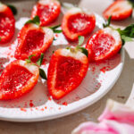 Champagne strawberry jello shots made with halved strawberries, glossy red centers, and sugar sprinkles on a white plate.