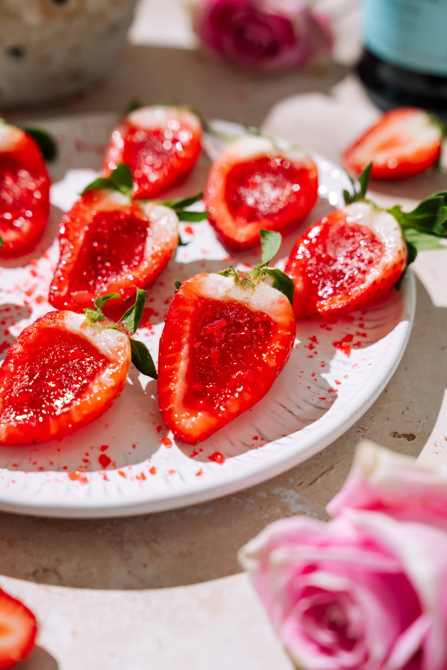 Champagne strawberry jello shots made with halved strawberries, glossy red centers, and sugar sprinkles on a white plate.