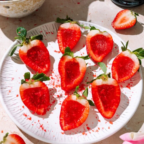 Champagne strawberry jello shots arranged on a white plate with fresh strawberries, pink roses, and a prosecco bottle.