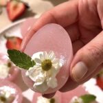 Close-up of pink Easter egg jello shot topped with whipped cream, chamomile flower, and mint leaf.