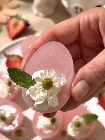 Close-up of pink Easter egg jello shot topped with whipped cream, chamomile flower, and mint leaf.
