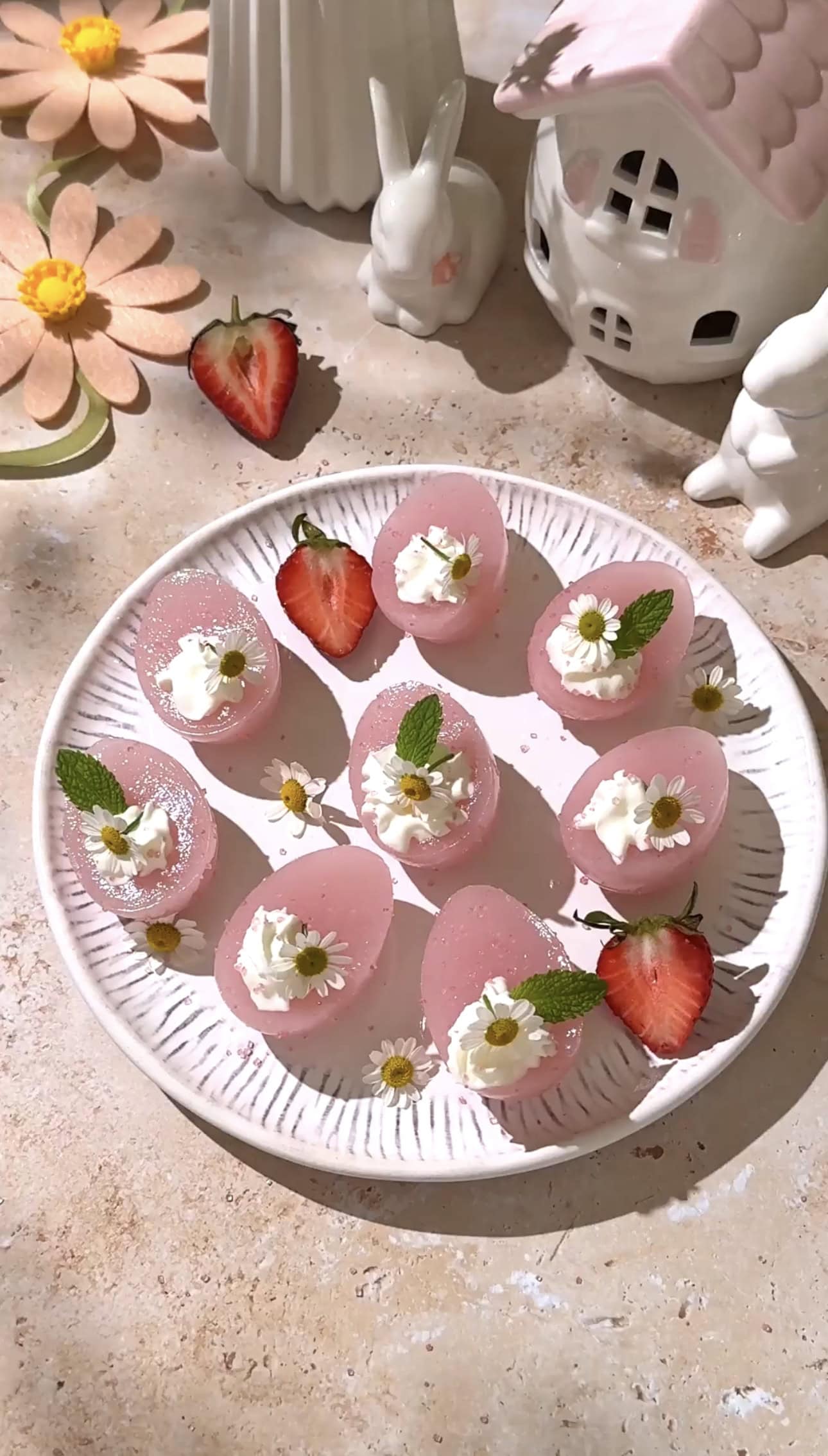 Plate of pink Easter egg jello shots topped with whipped cream, mint, and chamomile flowers.