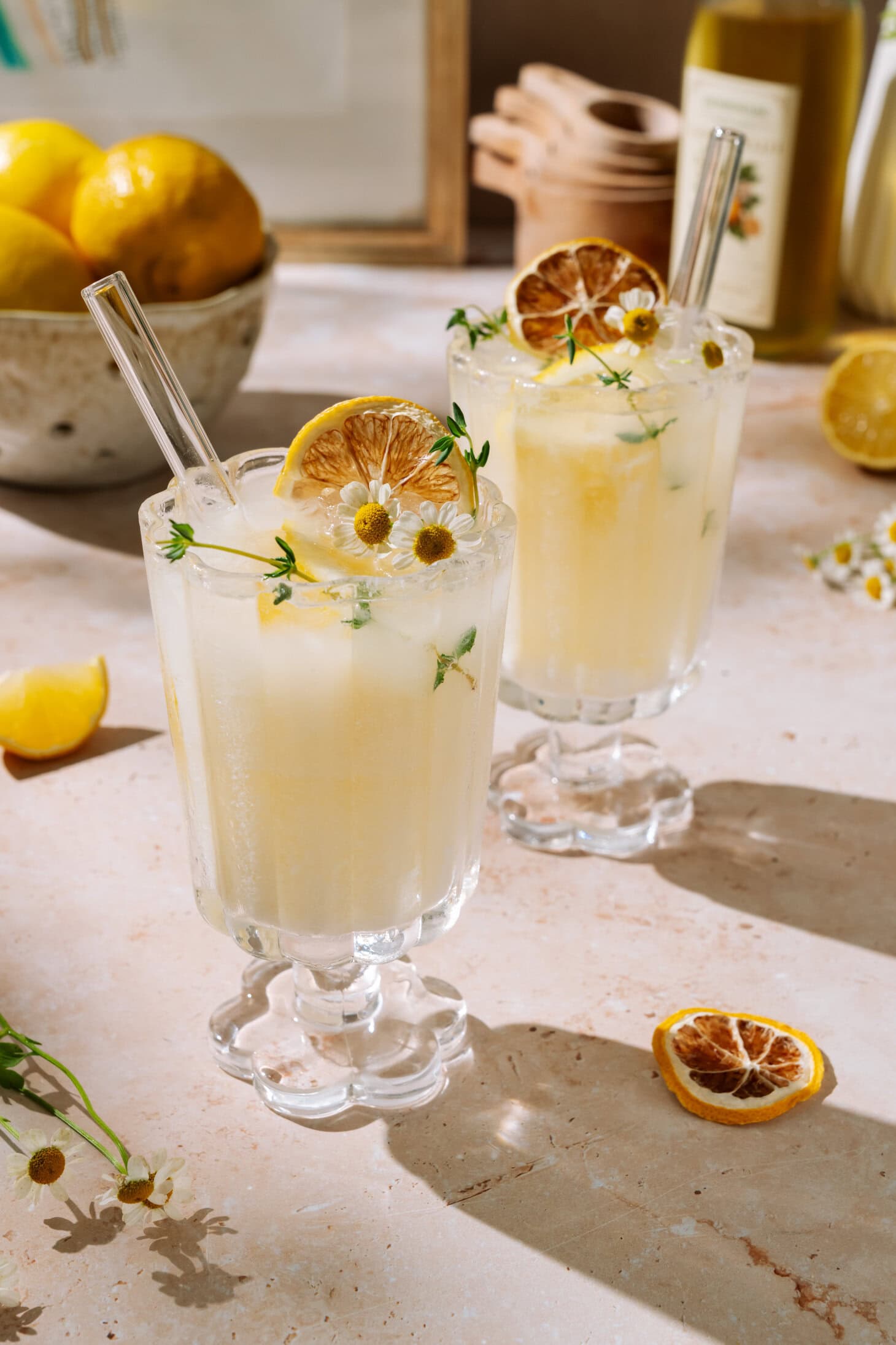 Two creamy limoncello spritz drinks garnished with dried lemon, herbs, and flowers on a light surface