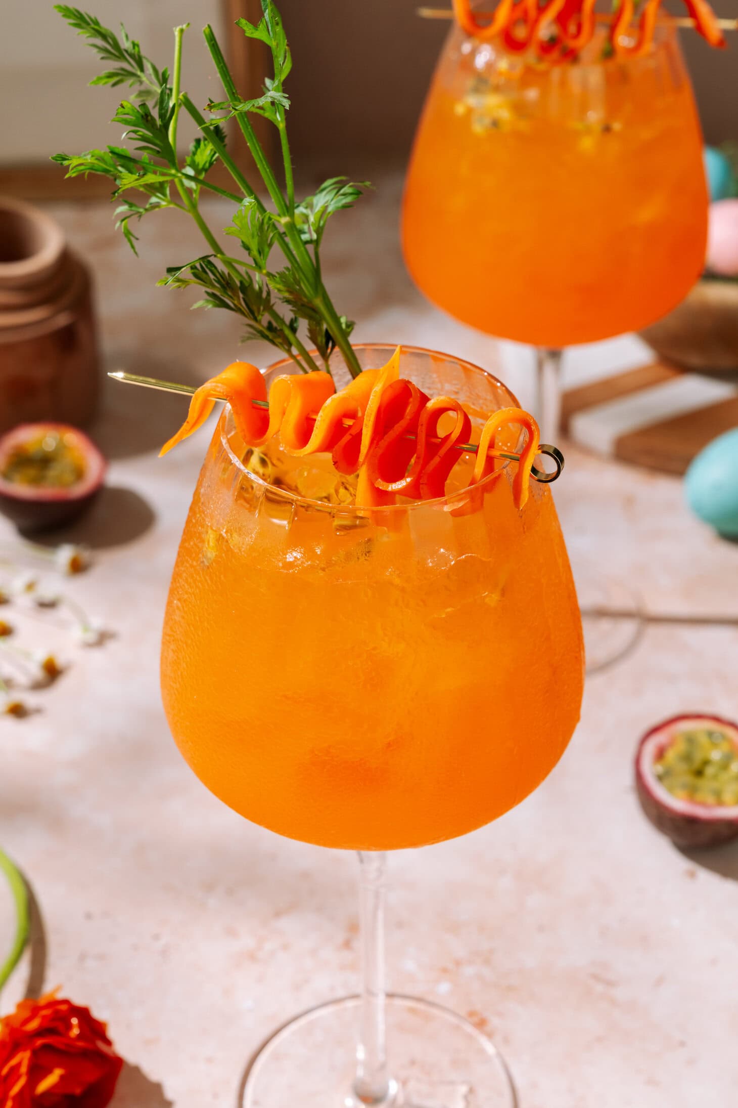 Passion Fruit Spritz cocktail with carrot ribbon garnish and fresh herbs in wine glasses.