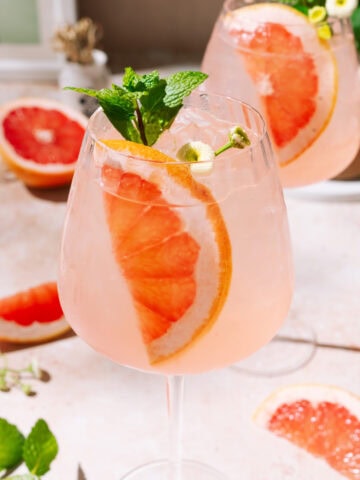Close up of Elderflower Grapefruit Spritz cocktail with fresh grapefruit garnish in a wine glass.