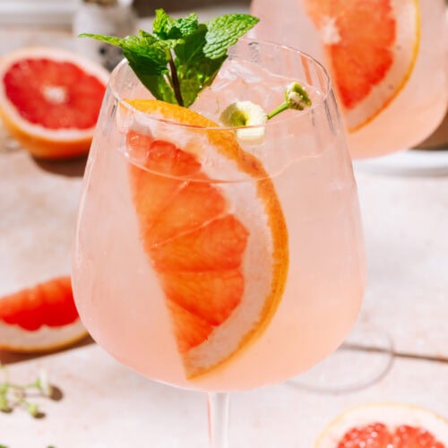 Close up of Elderflower Grapefruit Spritz cocktail with fresh grapefruit garnish in a wine glass.