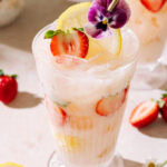 Creamy Strawberry Rhubarb mocktail with fresh strawberries, lemon, crushed ice, and edible flower garnish.