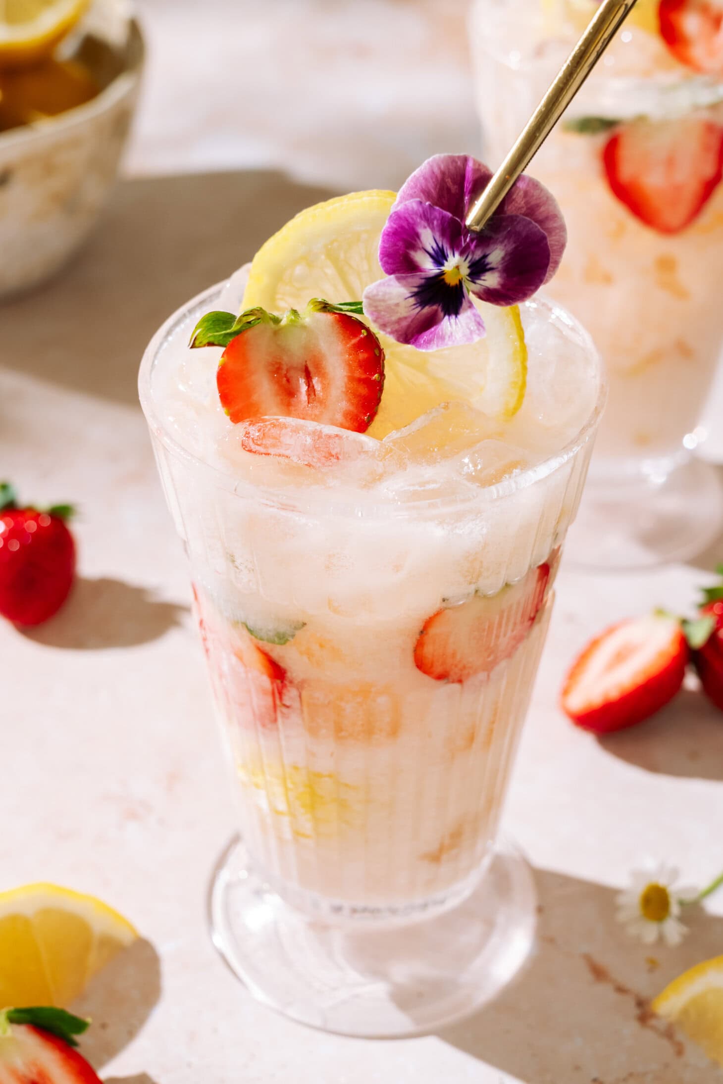 Creamy Strawberry Rhubarb mocktail with fresh strawberries, lemon, crushed ice, and edible flower garnish.