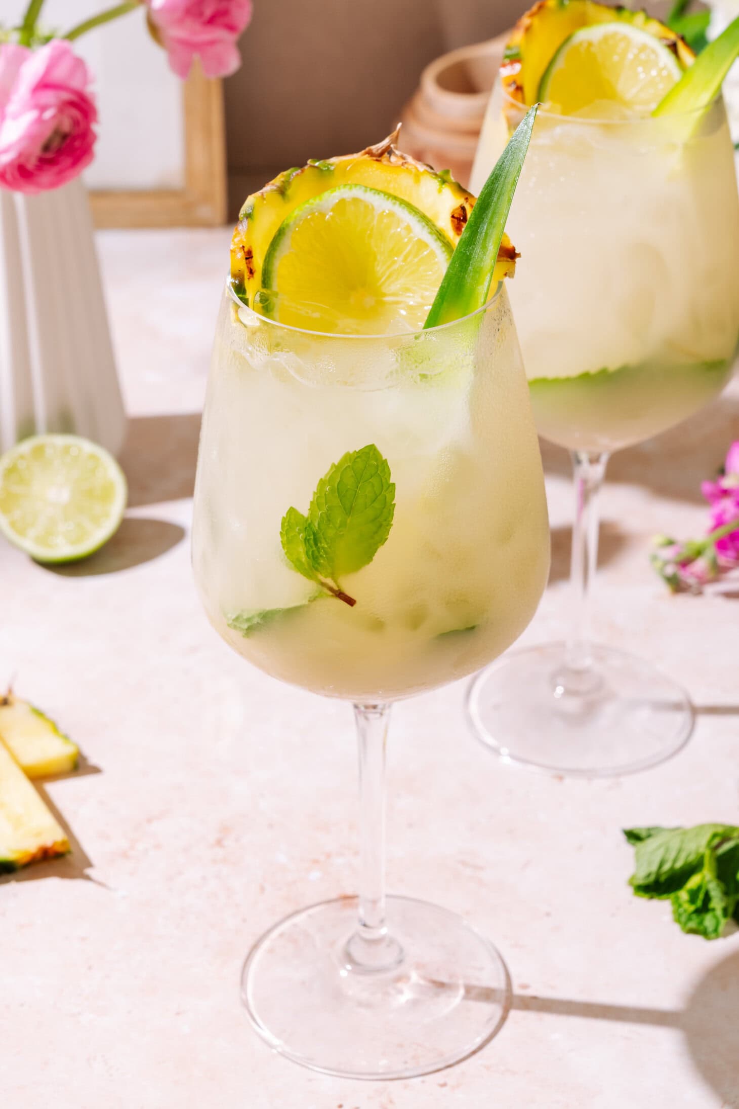 Piña Colada Hugo Spritz served in a tall wine glass with pineapple, lime, fresh mint, and tropical garnish served over ice.