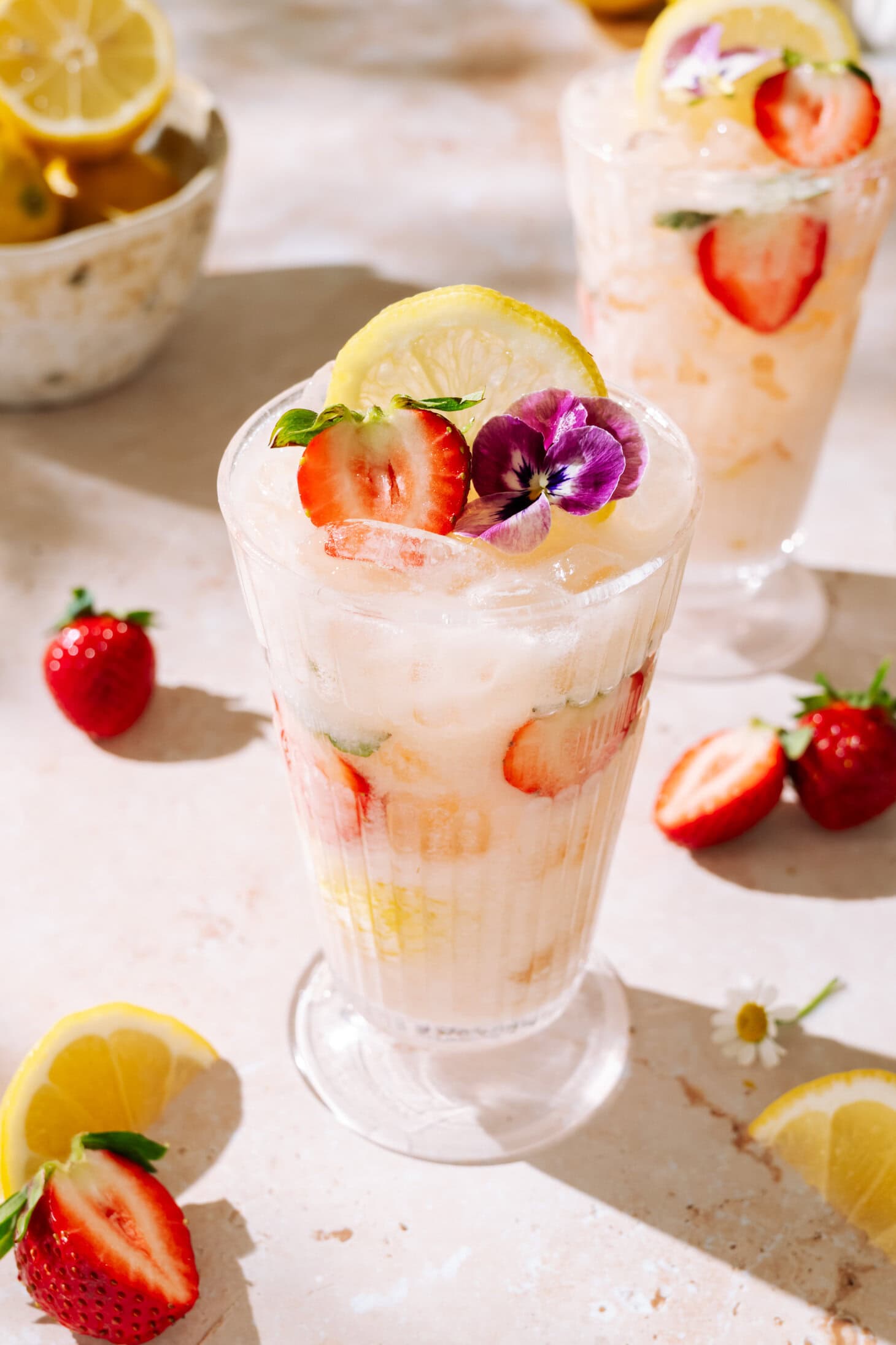 Creamy Strawberry Rhubarb mocktail with fresh strawberries, lemon, crushed ice, and edible flower garnish.