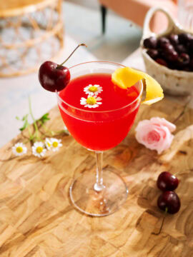 Cherry Bee’s Knees mocktail garnished with fresh cherries, lemon peel, and delicate chamomile flowers.