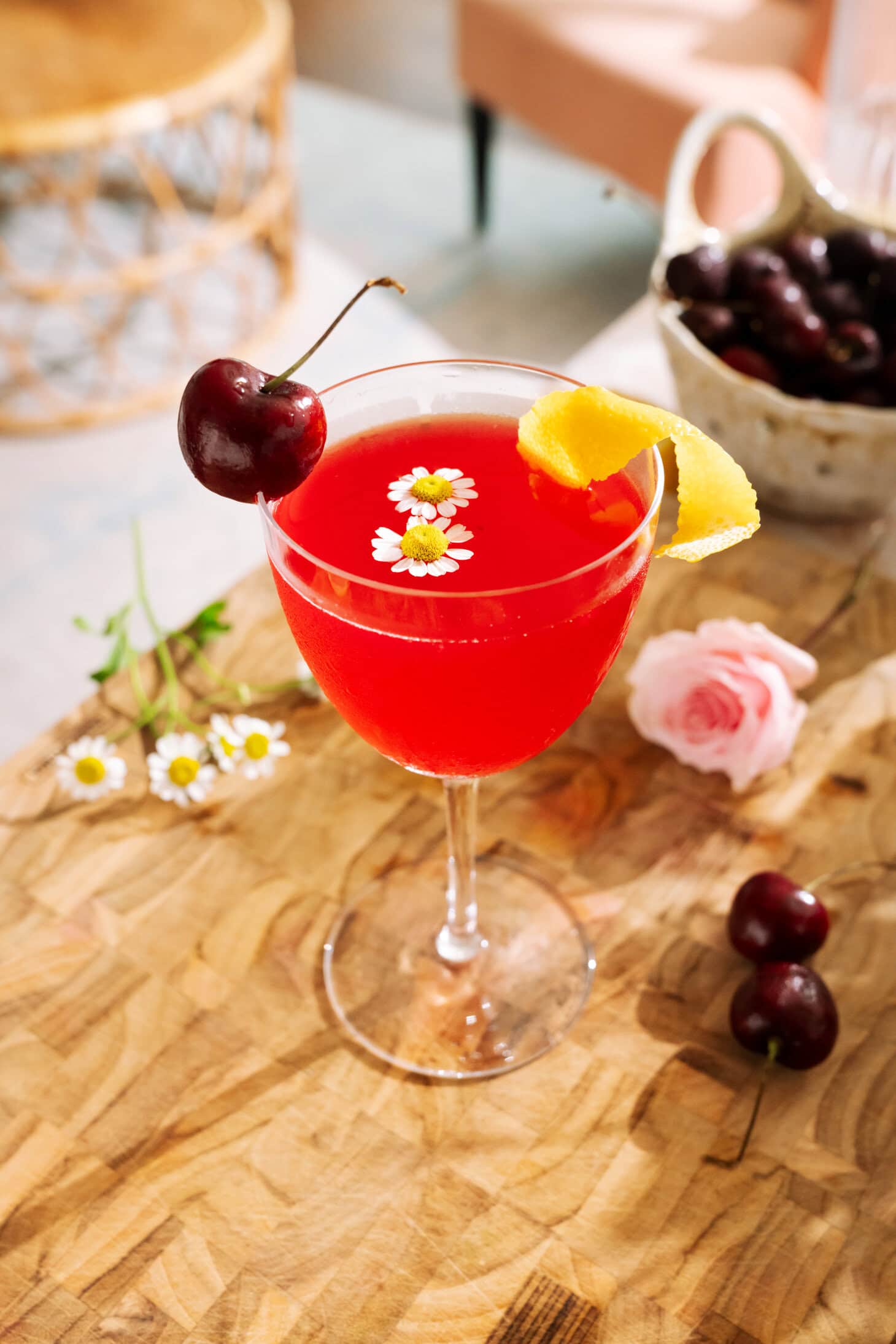 Cherry Bee’s Knees mocktail garnished with fresh cherries, lemon peel, and delicate chamomile flowers.