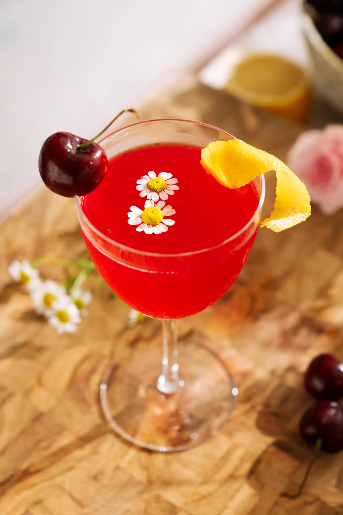 Cherry Bee’s Knees mocktail garnished with fresh cherries, lemon peel, and delicate chamomile flowers.