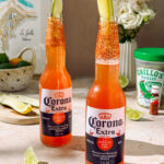 Refreshing Clamato michelada with lime, chili-salt rim, and pickle garnish in a chilled beer bottle, perfect for a spicy, tangy summer drink.