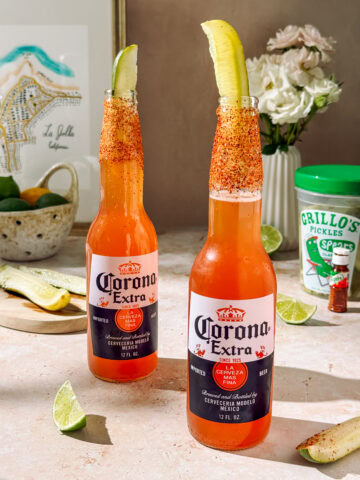 Refreshing Clamato michelada with lime, chili-salt rim, and pickle garnish in a chilled beer bottle, perfect for a spicy, tangy summer drink.