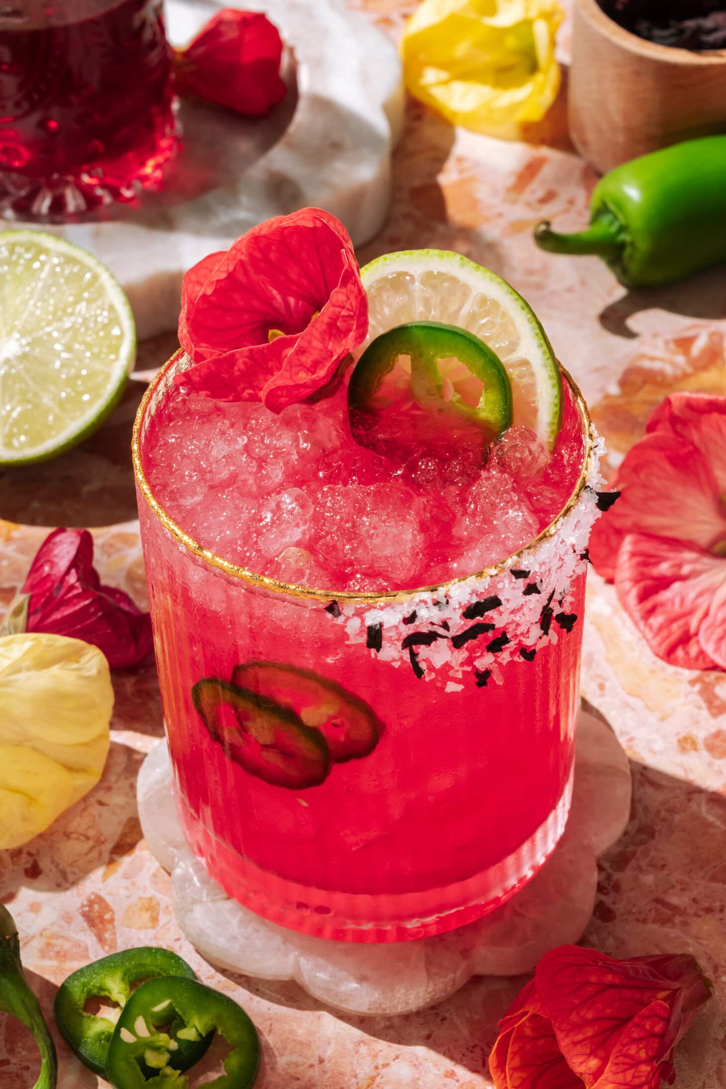 Vibrant spicy hibiscus margarita with lime, jalapeño slices, and edible flower garnish, served over crushed ice in a salt-rimmed glass.