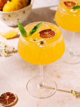 Bright and refreshing Ginger Peach Mocktail with fresh mint, dried orange slice, and edible flowers, served over ice in a stylish coupe glass.