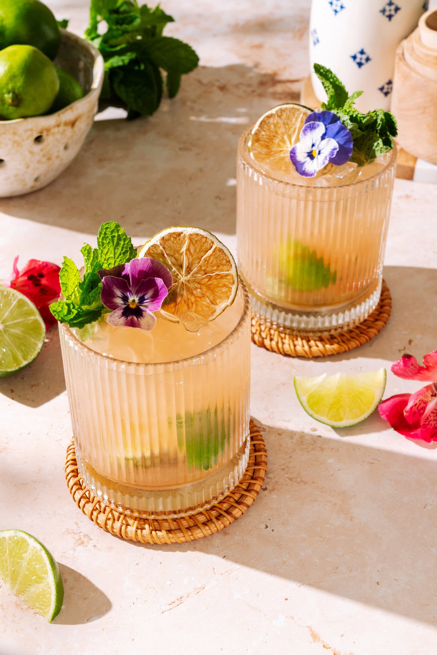 Two glasses of Guava Caipirinha cocktail with lime, fresh mint, dried citrus, and edible flower garnish.