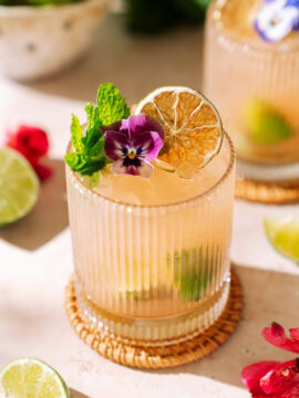 Guava Caipirinha cocktail with lime, fresh mint, dried citrus, and edible flower garnish.