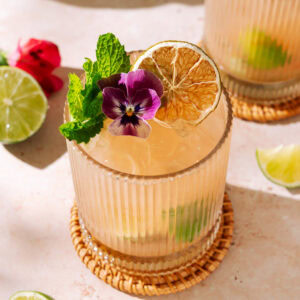 Guava Caipirinha cocktail with lime, fresh mint, dried citrus, and edible flower garnish.