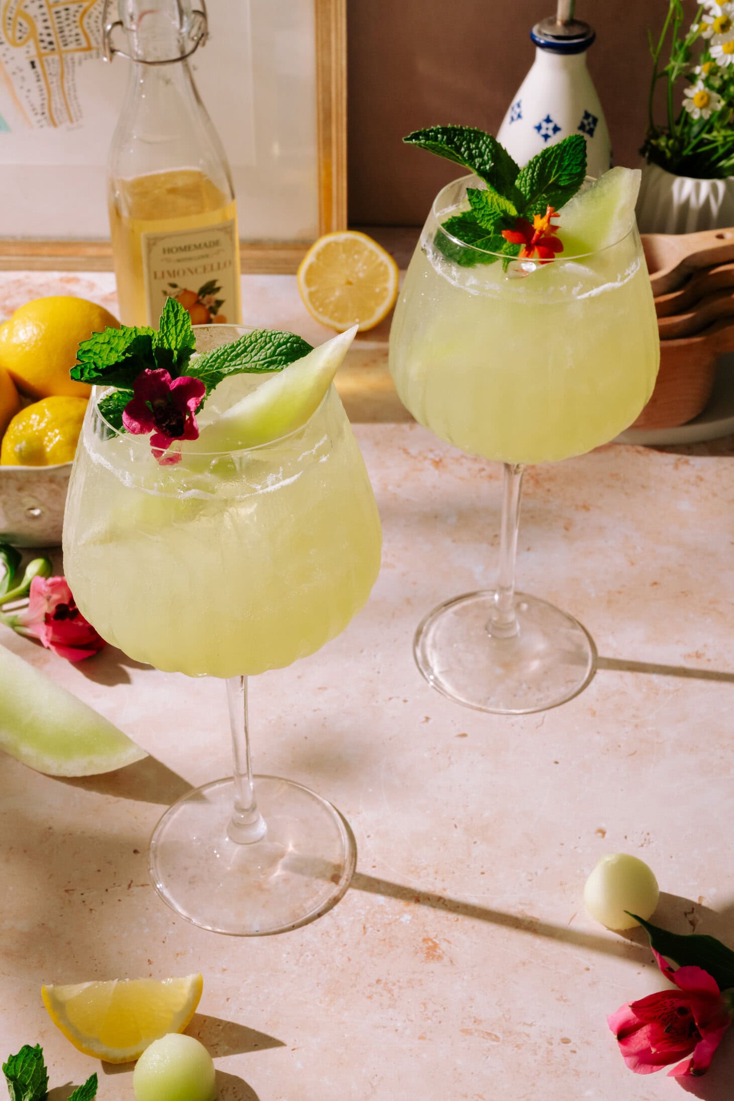 Two tall glasses of Honeydew Spritz with Limoncello, garnished with fresh mint, honeydew melon balls, and an edible flower.