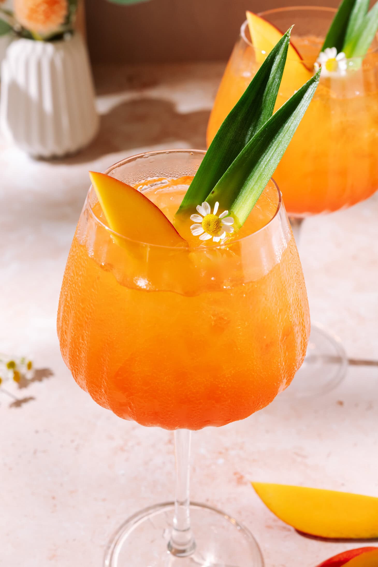 Aperol Mango Spritz with fresh mango slices, tropical leaf garnish, and edible flowers over ice.