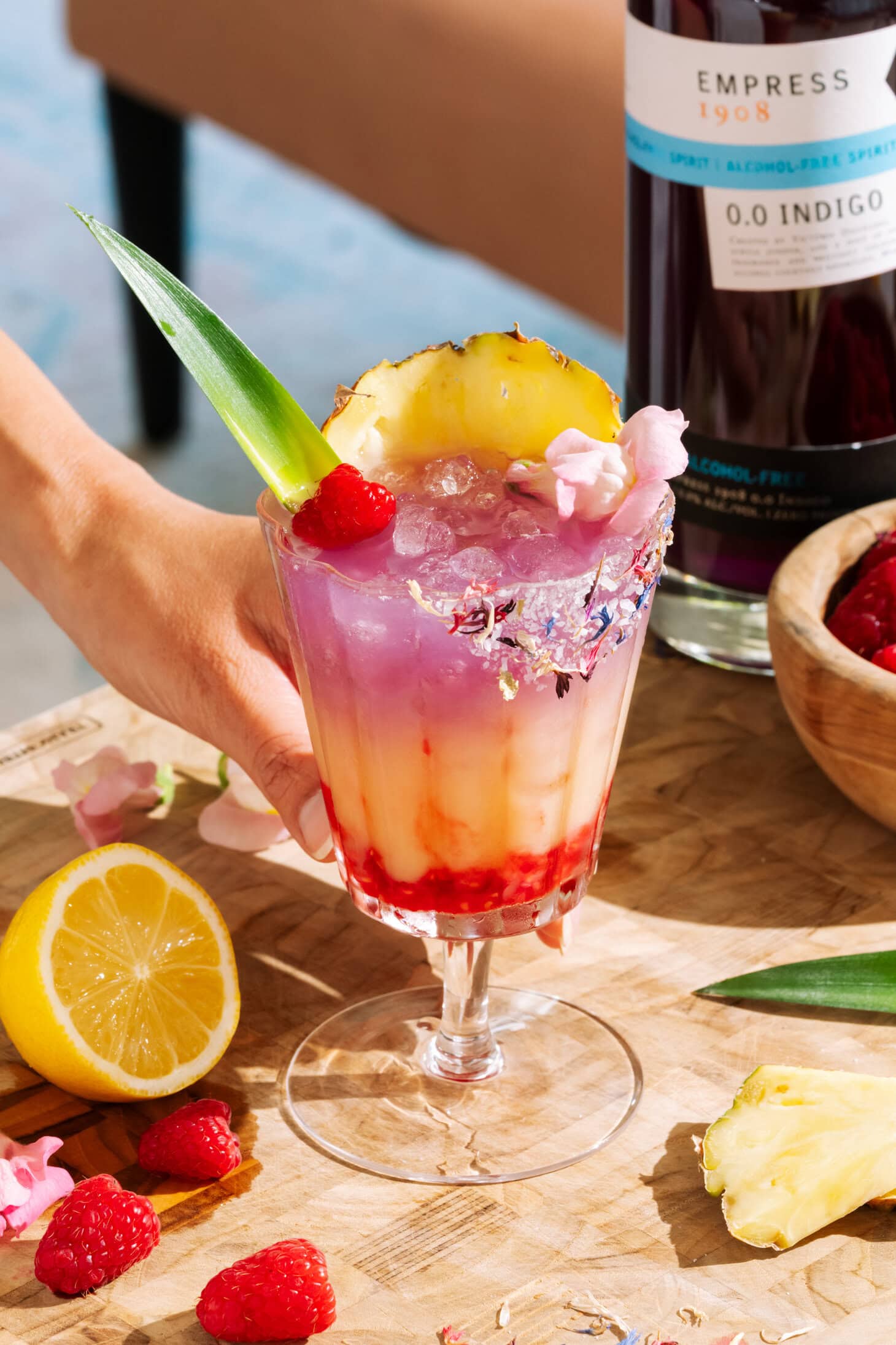 Raspberry Getaway Mocktail in a short glass garnished with fresh raspberries, pineapple, and pink flowers.