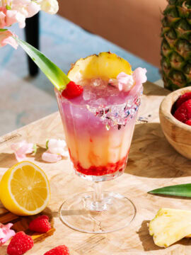 Raspberry Getaway Mocktail in a short glass garnished with fresh raspberries, pineapple, and pink flowers.