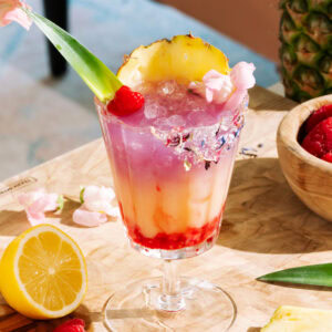 Raspberry Getaway Mocktail in a short glass garnished with fresh raspberries, pineapple, and pink flowers.