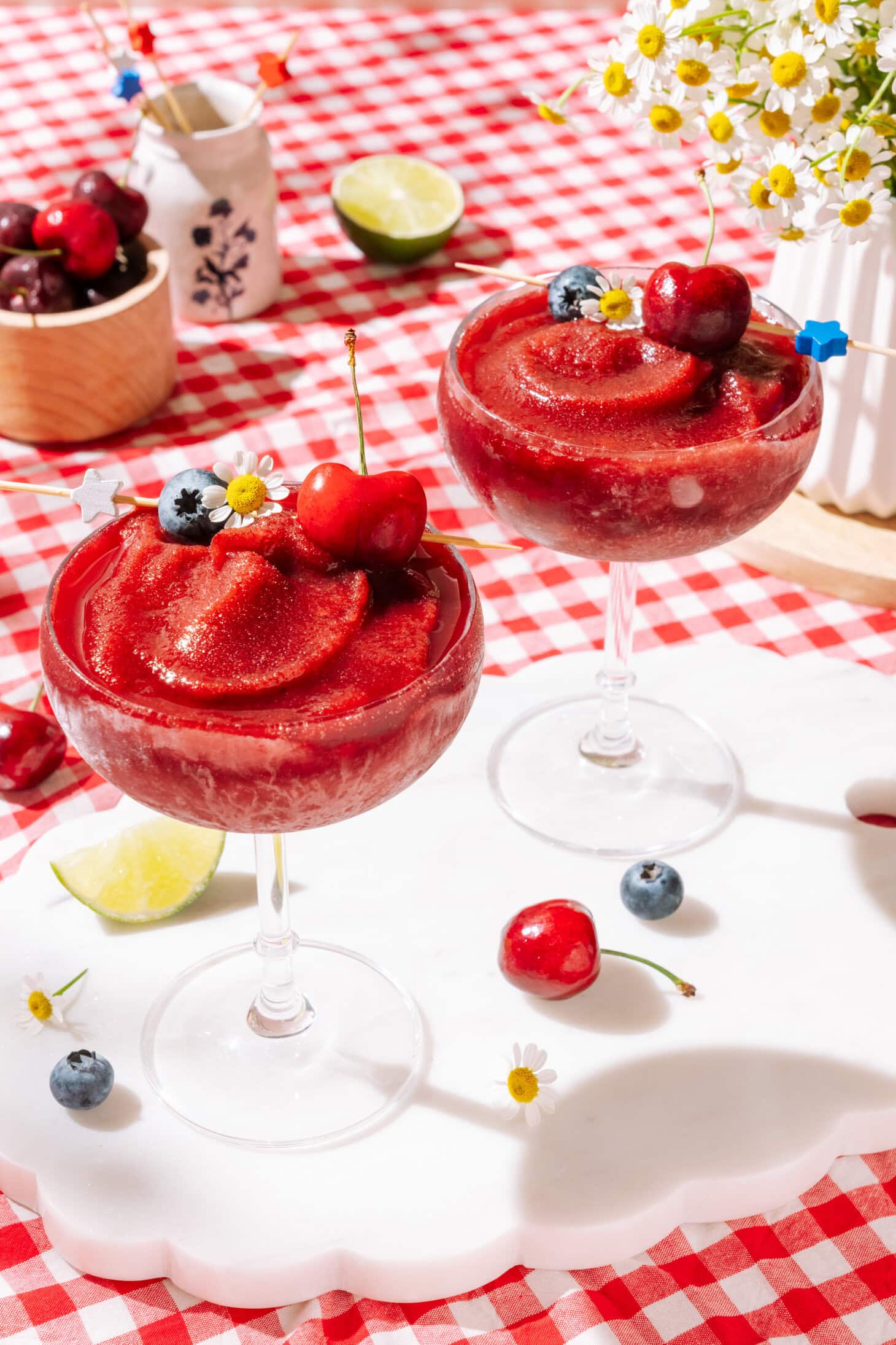 Spiked Cherry Slushy garnished with fresh cherries, blueberries, lime, and daisy flowers.