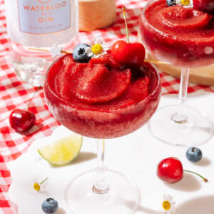 Spiked Cherry Slushy garnished with fresh cherries, blueberries, lime, and daisy flowers.