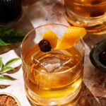 Añejo Tequila Old Fashioned cocktail in a short glass over ice, garnished with an orange twist and cherry.