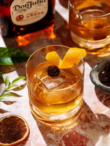 Añejo Tequila Old Fashioned cocktail in a short glass over ice, garnished with an orange twist and cherry.