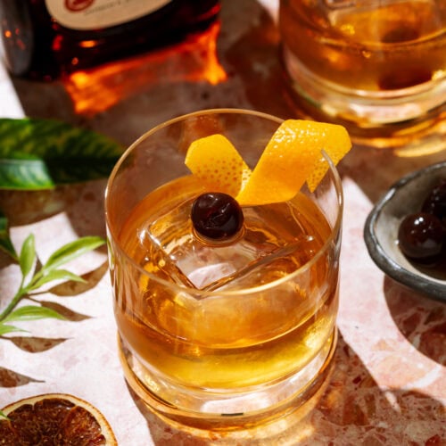 Añejo Tequila Old Fashioned cocktail in a short glass over ice, garnished with an orange twist and cherry.