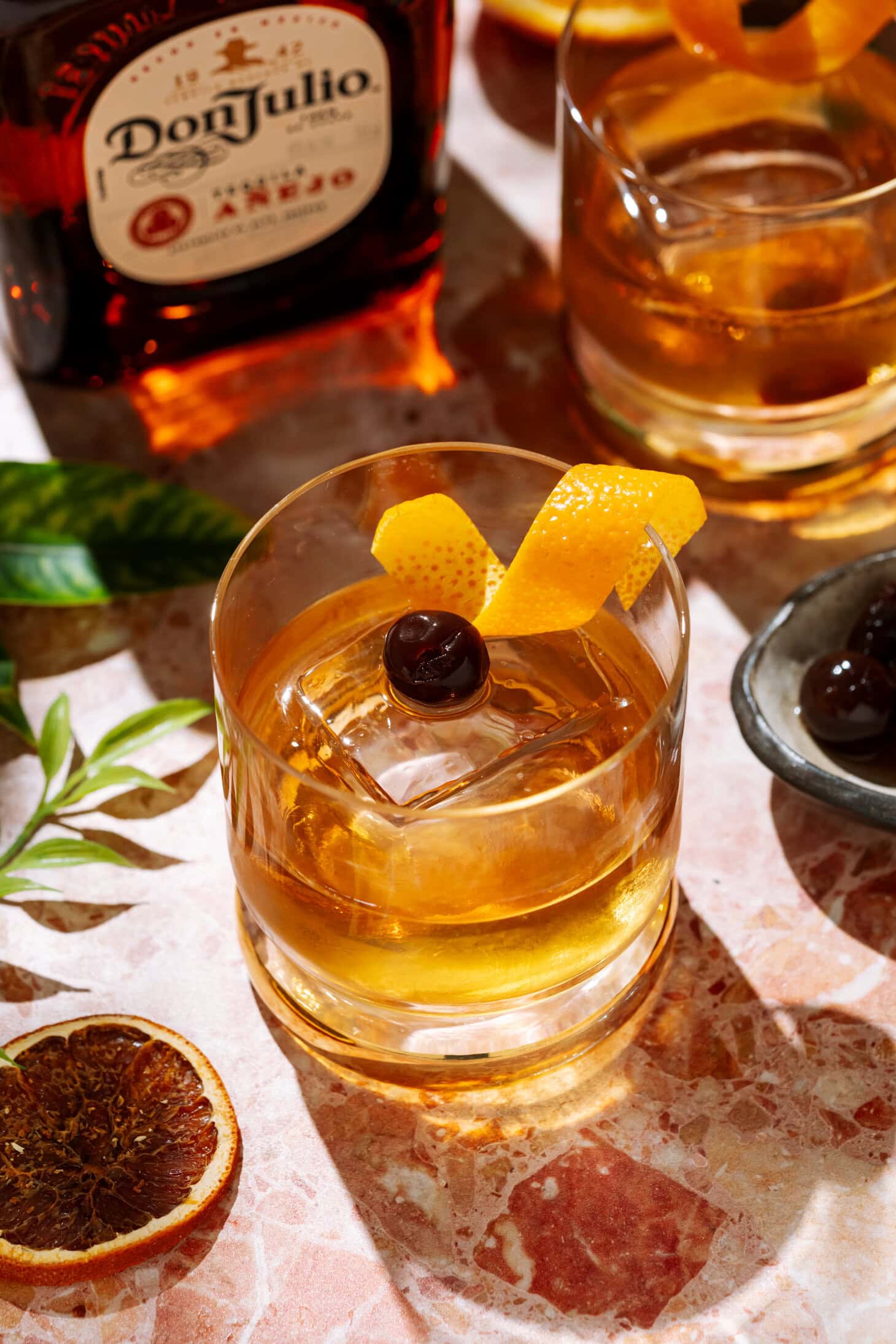 Añejo Tequila Old Fashioned cocktail in a short glass over ice, garnished with an orange twist and cherry.