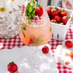 Easy Strawberry Spritz in a tall glass, decorated by mint and strawberries and with more strawberries and daisies in the background.