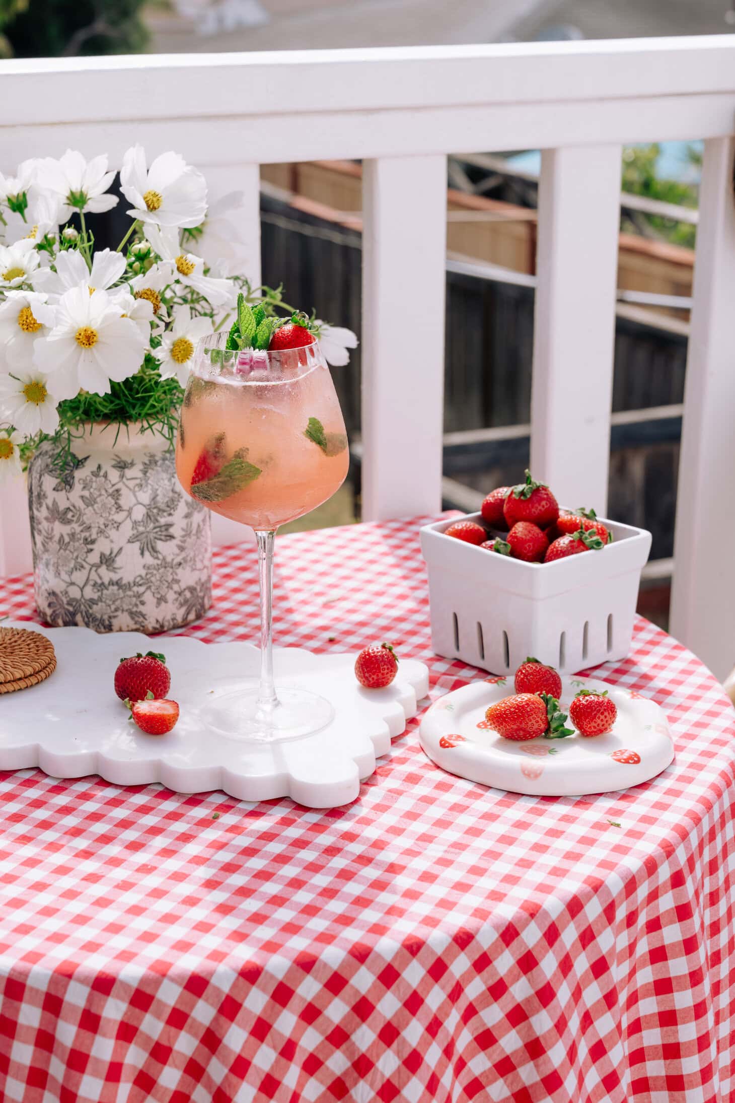 Easy Strawberry Spritz in a tall glass, decorated by mint and strawberries and with more strawberries and daisies in the background.