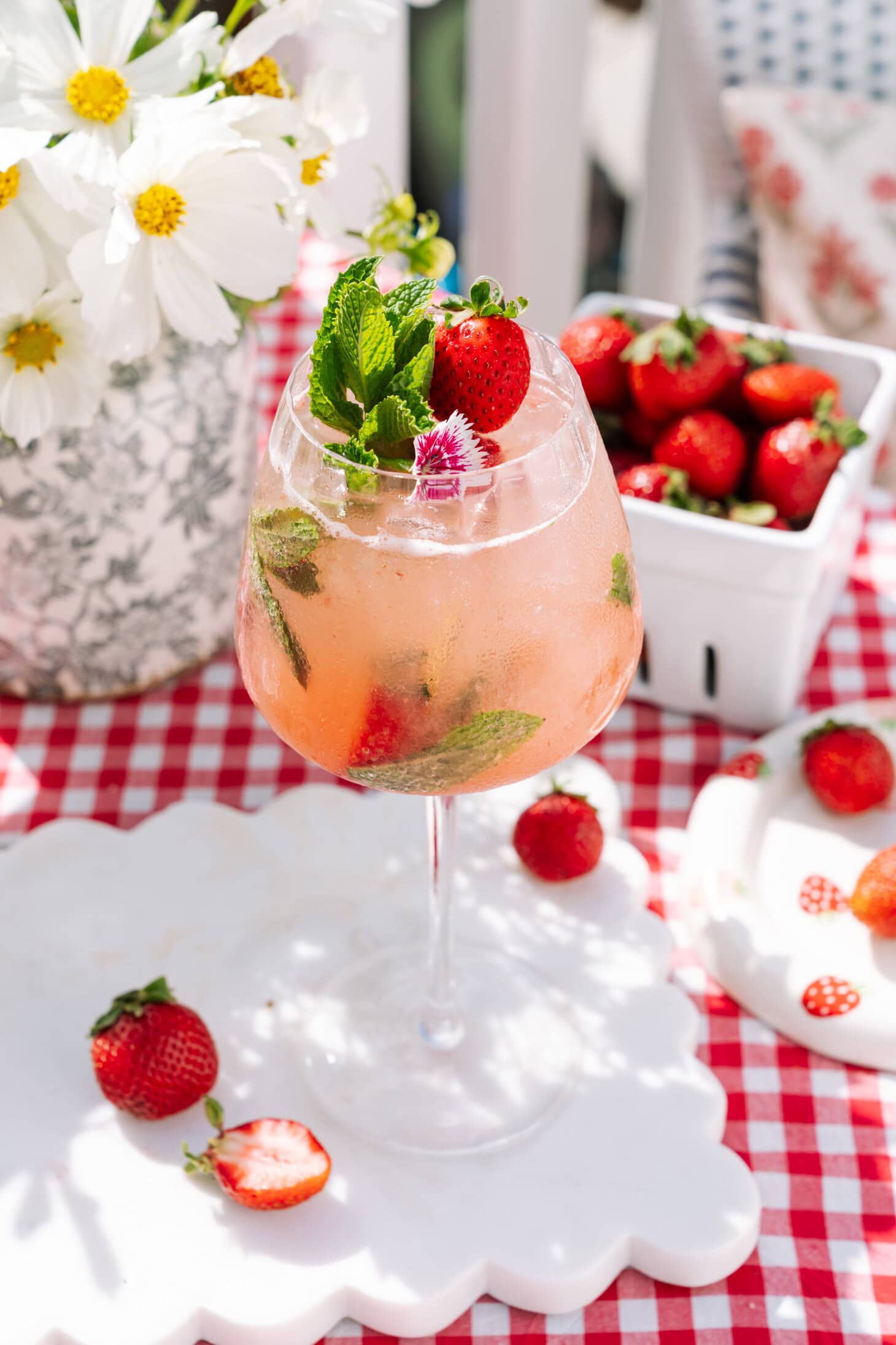 Easy Strawberry Spritz in a tall glass, decorated by mint and strawberries and with more strawberries and daisies in the background.