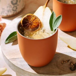 A close-up of a Amaretto Pear Margarita in a terracotta cup, garnished with pear slices and dried citrus on a wooden board.