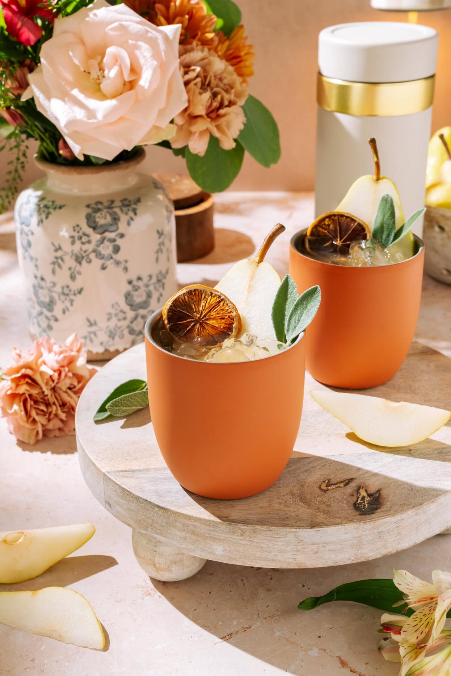 Amaretto Pear Margaritas in a terracotta cup, garnished with pear slices and dried citrus on a wooden board.