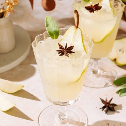 Pear White Wine Spritzer in stemmed glasses, garnished with fresh pear, sage, and star anise.
