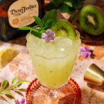 Tequila Kiwi Cocktail in a stemmed glass, garnished with fresh kiwi, mint, and a purple flower.