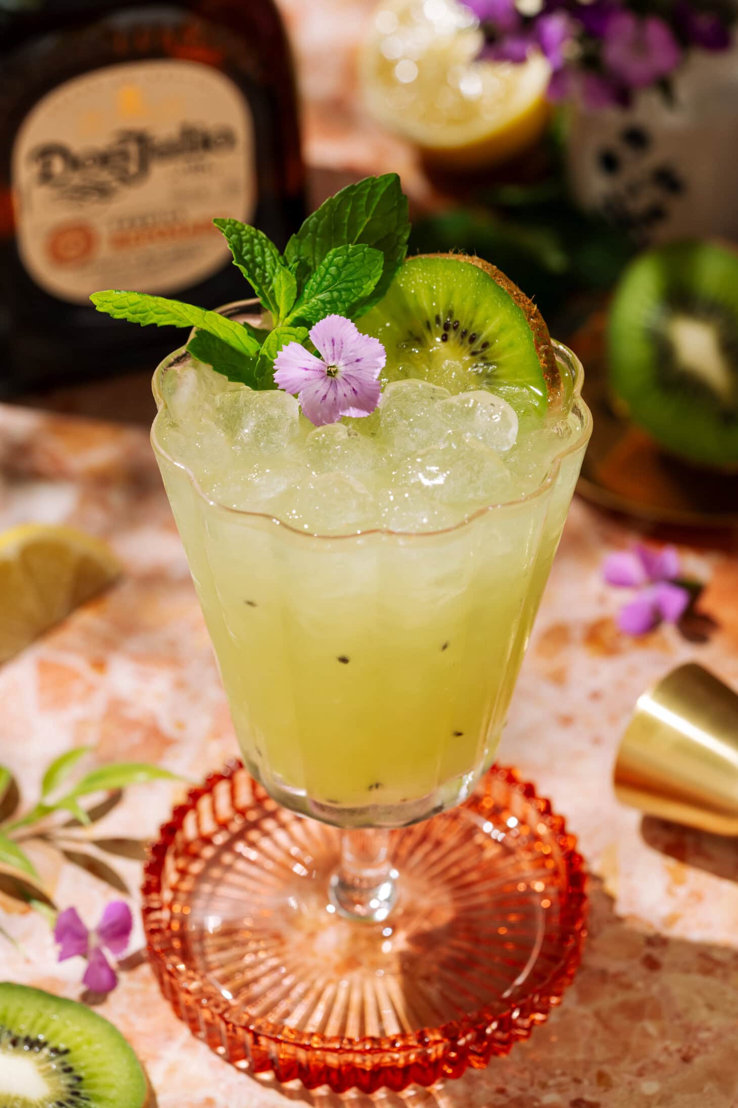 Tequila Kiwi Cocktail in a stemmed glass, garnished with fresh kiwi, mint, and a purple flower.