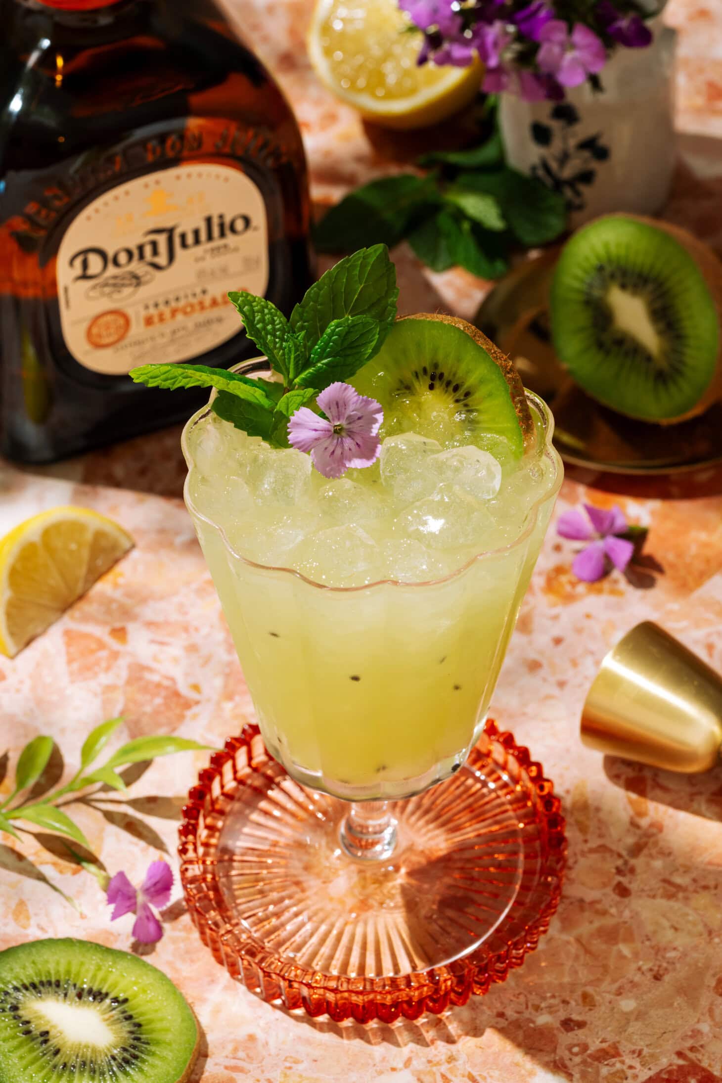 Tequila Kiwi Cocktail in a stemmed glass, garnished with fresh kiwi, mint, and a purple flower.