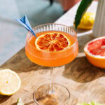Vibrant orange cocktail in tall glass with dried citrus slice garnish on a wooden table.