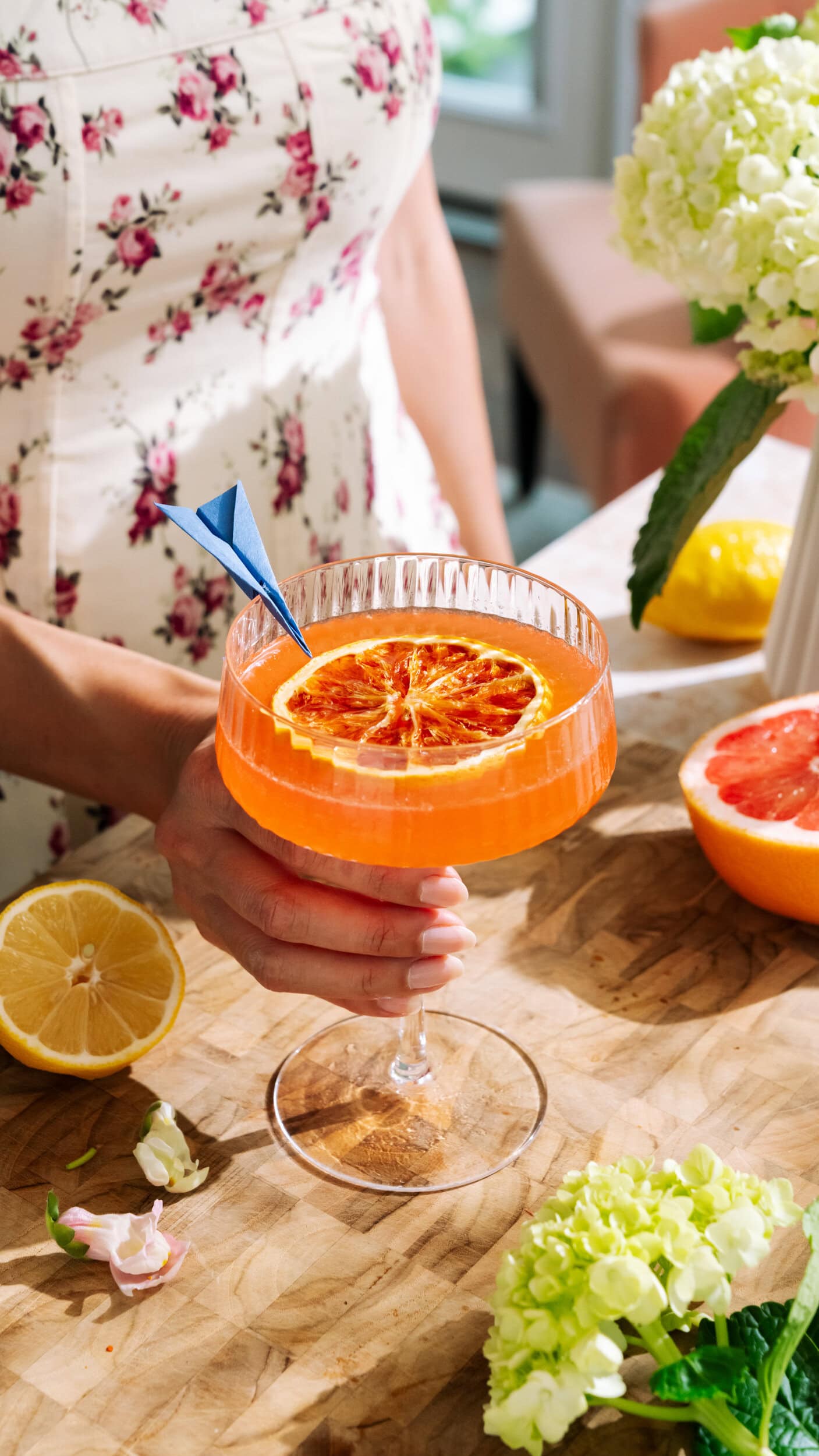 Vibrant orange cocktail in tall glass with dried citrus slice garnish on a wooden table.