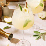 Two pear cocktails garnished with green leaves, served in elegant glasses on a stylish bar counter.