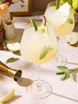 Two pear cocktails garnished with green leaves, served in elegant glasses on a stylish bar counter.