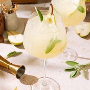 Two pear cocktails garnished with green leaves, served in elegant glasses on a stylish bar counter.