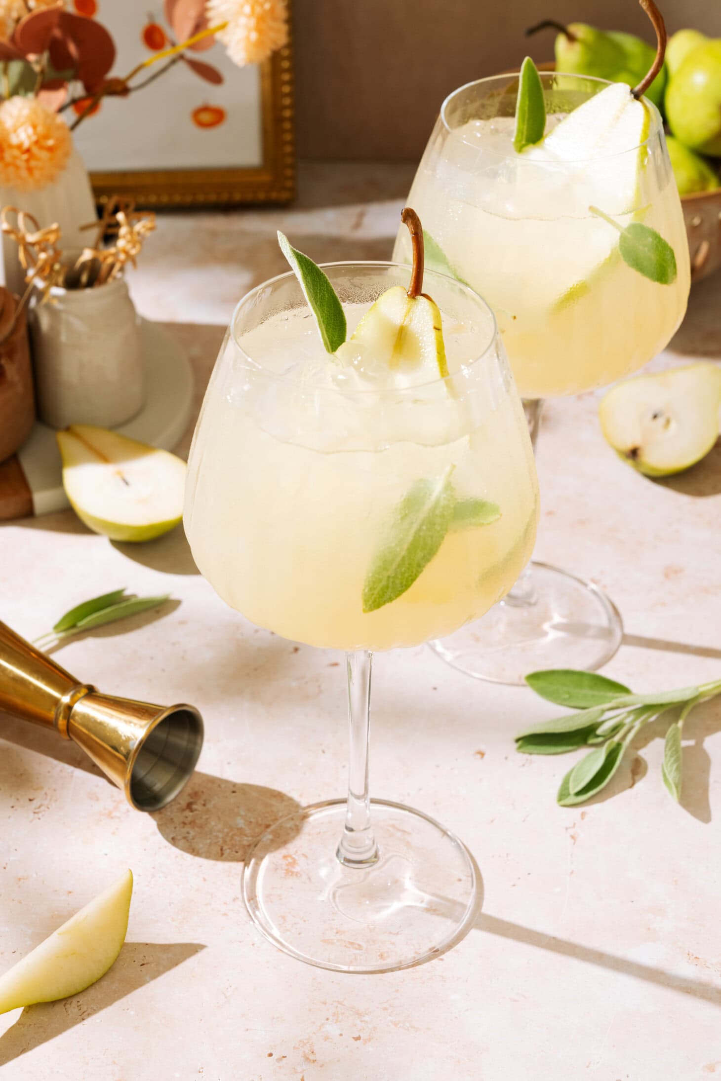 Two pear cocktails garnished with green leaves, served in elegant glasses on a stylish bar counter.